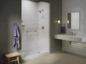 A bathroom with grey walls and a walk-in shower with a white surround and safety features 